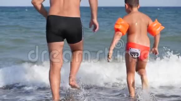 海滩暑假一个男人和一个孩子跑进汹涌的大海里潜水视频的预览图