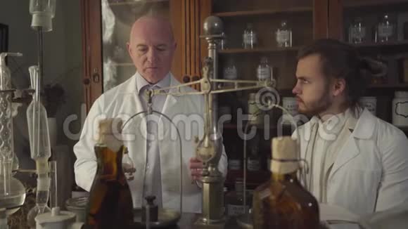快乐的老白种人展示老式试管和瓶子给年轻人和交谈穿白袍的药剂师视频的预览图