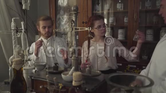 三个白人药剂师谈话的肖像站在古代药店里拿着试管烧瓶和视频的预览图