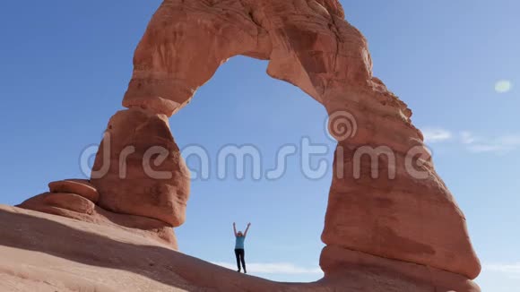 游客举起双手站在国家公园内一座精致的橙色岩石拱门中视频的预览图