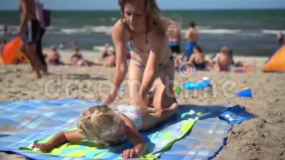 嬉戏的妈妈在沙滩上为她的小女儿做按摩视频的预览图