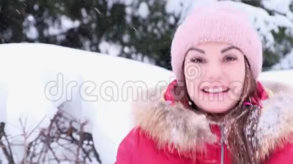 一个快乐的年轻女子在冬天散步时吐雪在飘落的雪中快乐视频的预览图