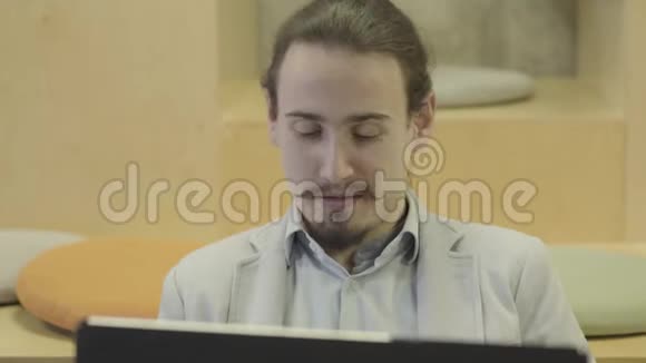 一个年轻的白人男子的特写肖像带胡子和胡须看着笔记本电脑积极的商人在网上工作视频的预览图
