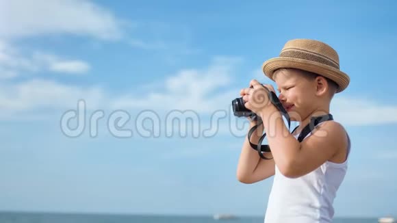 快乐旅行小男孩戴帽子在蓝天背景下用相机拍摄海景视频的预览图