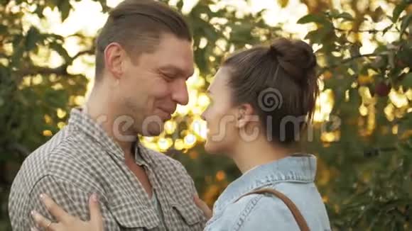 快乐的男人和女孩在公园日落时亲吻和拥抱在苹果园浪漫的环境中爱男人和女人视频的预览图