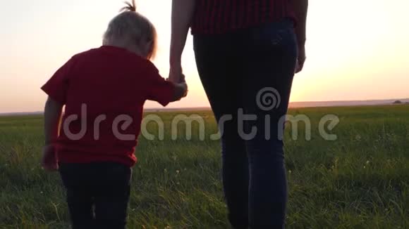 一位年轻的母亲牵着女儿手幸福的一家人在夕阳下的清新空气中散步视频的预览图