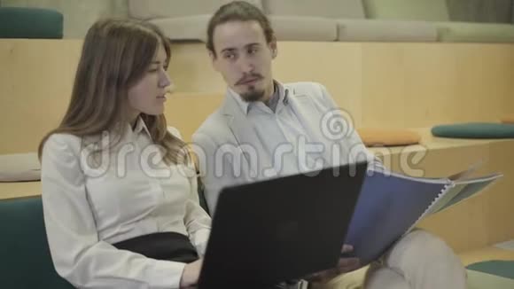 一对年轻的高加索男人和女人坐在笔记本电脑和文件和谈话讨论生意的同事视频的预览图