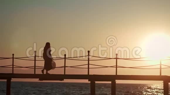 孤独的女旅行者在夕阳下漫步码头凝视美丽的海景伴着灿烂的阳光视频的预览图