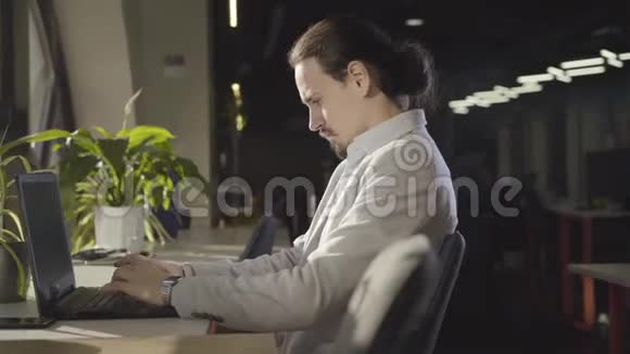 镜头在集中的白人男人周围移动晚上坐在空地上在笔记本电脑键盘上打字肖像视频的预览图