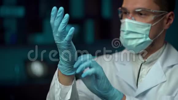 近距离观看严肃的年轻胡须男医生穿着白色职业外套戴上蓝色防护手套视频的预览图