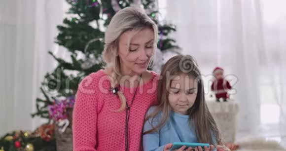 特写镜头年轻的白人母亲和女儿在智能手机屏幕上看电影或动画片装饰过的圣诞节视频的预览图