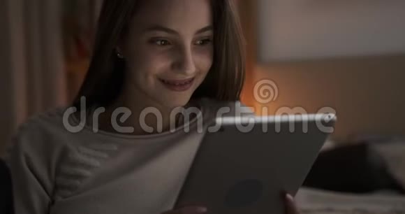晚上在数码平板电脑上欣赏媒体内容的少女视频的预览图