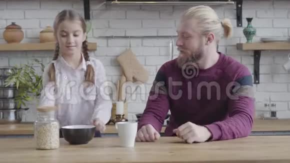 漂亮的白种人黑发女孩扎着辫子把玉米片倒进盘子里把它们送给父亲女儿视频的预览图