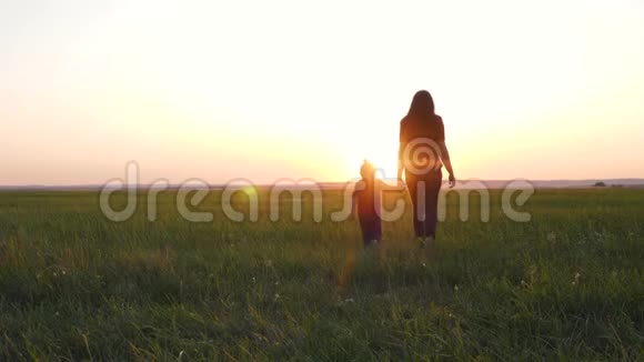 一位年轻的母亲牵着女儿手幸福的一家人在夕阳下的清新空气中散步视频的预览图