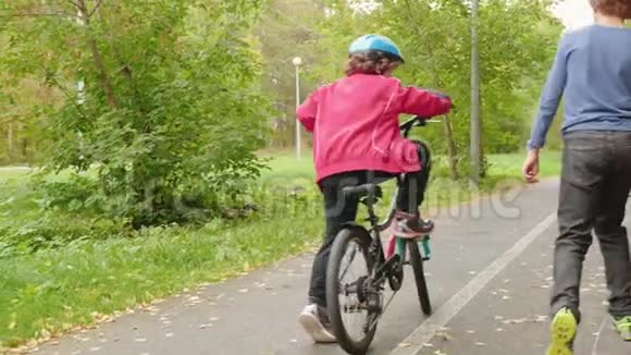 骑自行车的男孩骑自行车在秋季公园后景的道路上少年男孩骑在滑板上后视图二视频的预览图