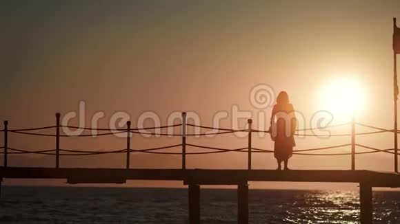 戴帽子的时尚女人站在海上的桥上欣赏日落视频的预览图