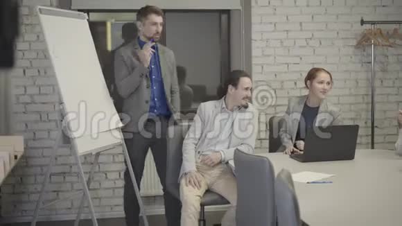 一个穿着灰色西装的白种人站在空地办公室的旁边和坐在办公室的同事交谈视频的预览图
