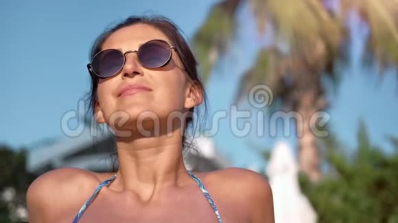 身着比基尼在海滩上享受日光浴的深色浅黑色微笑女人的近景皮肤视频的预览图