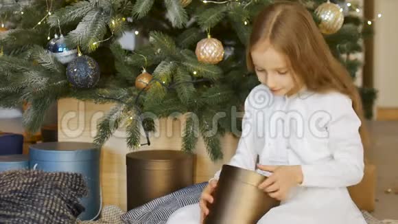 可爱的金发女孩打开了一个暗金礼盒她坐在圣诞树旁快乐的童年和圣诞节视频的预览图