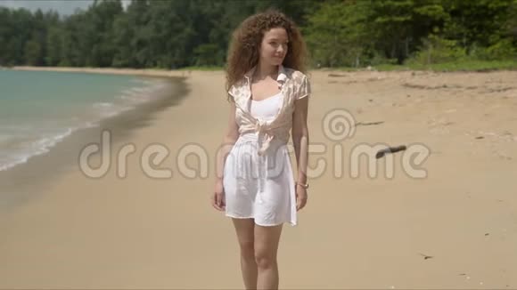 穿着夏装在阳光明媚的沙滩上散步的迷人女人视频的预览图