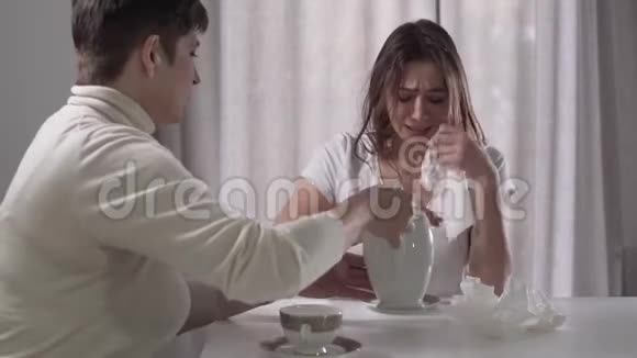 年轻美丽的高加索女人和妈妈坐在桌子旁哭泣的肖像一位深褐色头发的女士倒茶视频的预览图