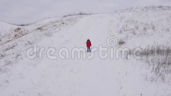 一个孩子走在白色的雪山上手里拿着雪橇冬季运动会寒冷的气候条件雪山视频的预览图
