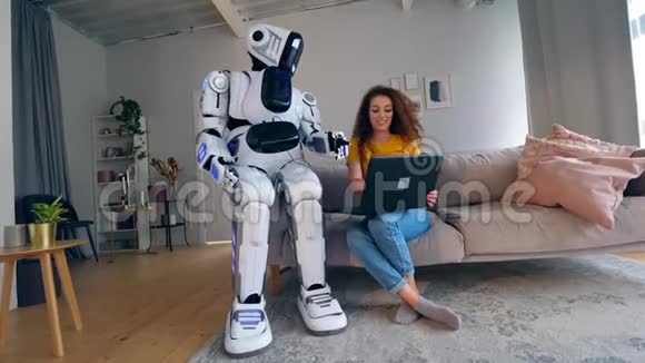 年轻的女人正在操作笔记本电脑和机器人说话机器人人形半机概念视频的预览图
