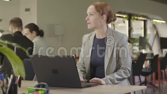 开朗的中年白种人女士坐在空地办公室戴上派对帽微笑着积极正面视频的预览图