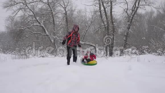 快乐的童年概念快乐的父母在圣诞公园里和他们的孩子玩爸爸骑着他女儿的雪橇视频的预览图