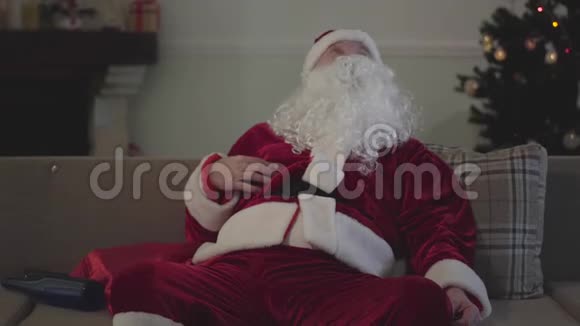 穿着圣诞老人服装坐在沙发上喝酒的醉汉孤独的白人独自度假视频的预览图