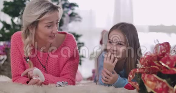 积极的白人母亲和女儿大声笑因为在家吃饼干女人和女孩躺在柔软的白色视频的预览图
