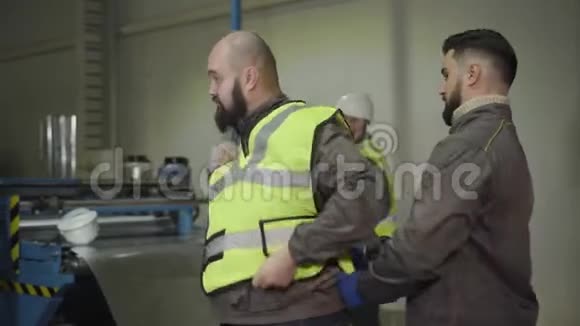 英俊的白种人工头帮助胡子工人穿上安全背心生产工厂的工人安全视频的预览图