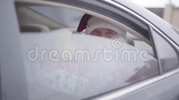 老圣诞老人打开车窗眨眼坐在后座上的有胡子的圣诞老人带着礼物盒视频的预览图