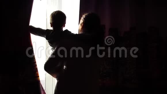 母亲早上在窗户附近抱着一个孩子清晨他们拉开窗帘阳光阳光照进来视频的预览图