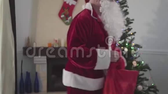 无法辨认的白人圣诞老人拿着他的礼品袋在圣诞树前跳舞节日快乐的概念视频的预览图