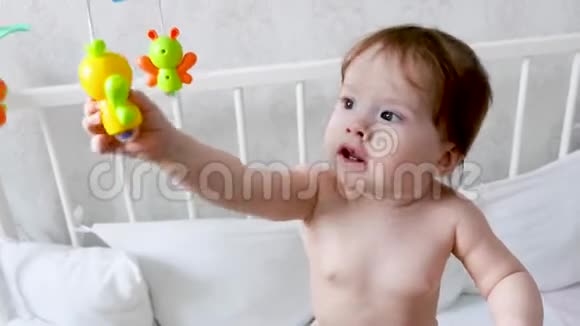 一个穿着尿布的快乐小孩子站在婴儿床上玩着玩具孩子的生活婴儿在儿童室玩耍视频的预览图