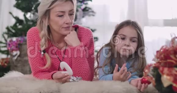 年轻的高加索母女躺在柔软的地毯上吃饼干的肖像成年妇女和小女孩视频的预览图