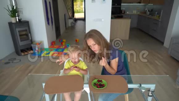 在玻璃桌旁吃樱桃浆果的金发小孩和白种人女人视频的预览图