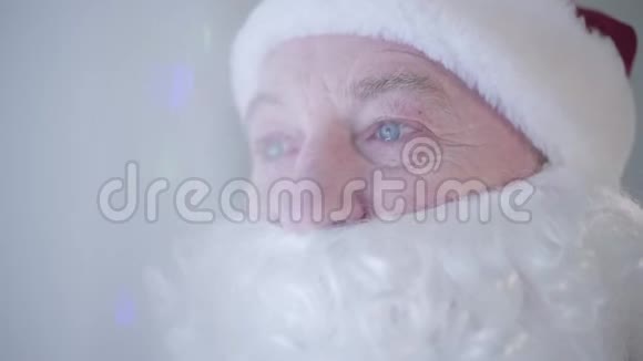 圣诞老人装扮成假胡子站在新年树前哭泣的老人的特写视频的预览图
