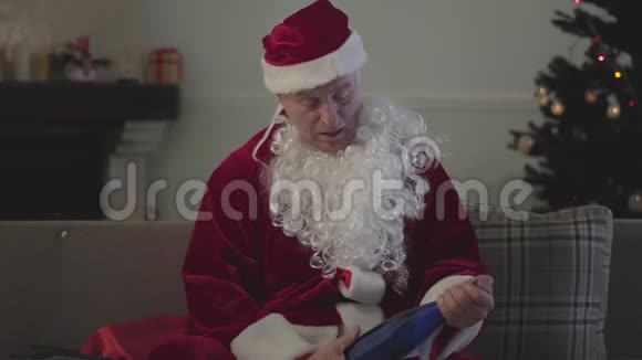 一个穿着圣诞老人服装坐在沙发上手里拿着空瓶子的死白种人成熟的男人倾吐视频的预览图