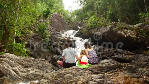 一家人爸爸妈妈女儿坐着欣赏瀑布美景视频的预览图