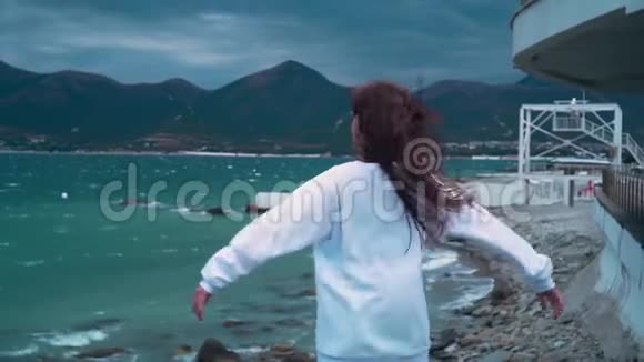 一个女孩在暴风雨中站在海滨她的背在框架里海边的女孩举起双手视频的预览图