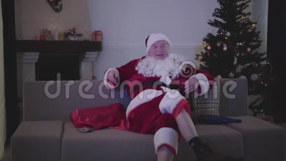 穿着圣诞老人衣服端着啤酒坐着看电视的成年白种人肖像酗酒的圣诞老人视频的预览图