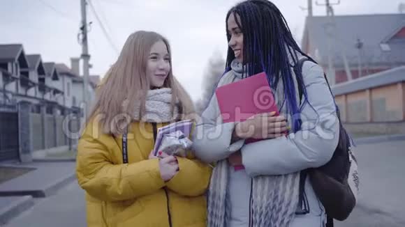 微笑的年轻女性朋友在街上散步聊天非洲裔美国人和白人女孩散步视频的预览图