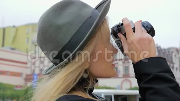一个年轻的白种人女人一个戴着帽子的时髦女郎在一台老式的摄像机上拍照概念记者博客作者视频的预览图