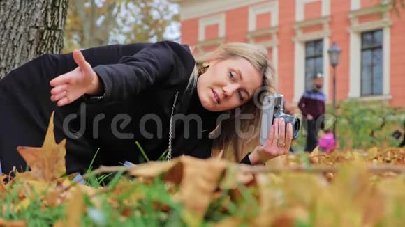 一位年轻的白人女摄影师在老式复古胶卷相机上拍摄秋季照片潮人拍得低视频的预览图