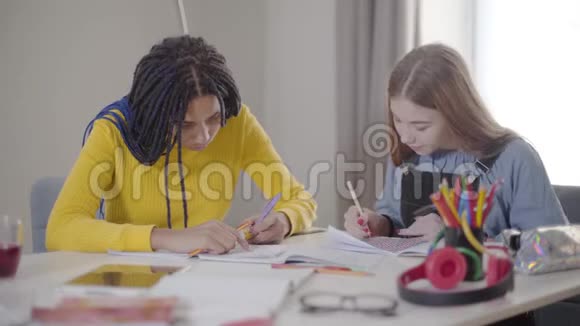 年轻的白种人金发女孩在笔记本上画画作为她的非裔美国朋友写作两个可爱的朋友视频的预览图