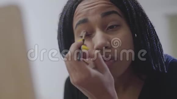 非洲裔美国少女涂眼影的特写镜头戴着可怕的锁看着镜子视频的预览图