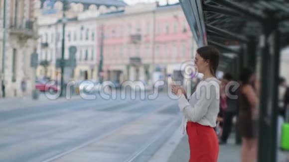 女人用智能手机站在城市的电车站上视频的预览图