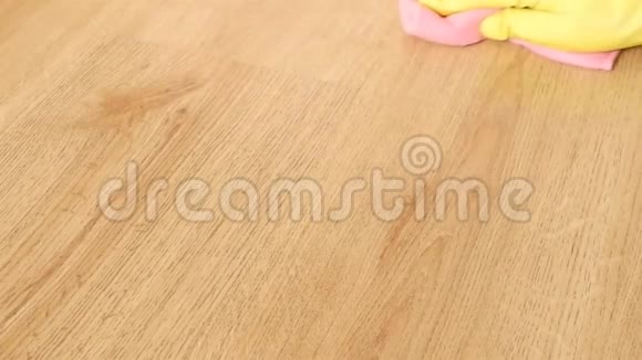 女性手在黄色橡胶手套特写洗木地板与粉红色的微纤维布视频的预览图
